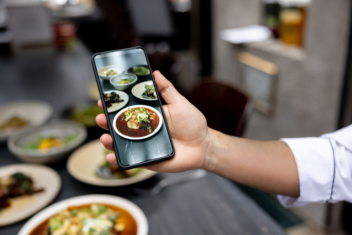 Hand holding smartphone taking picture of food.