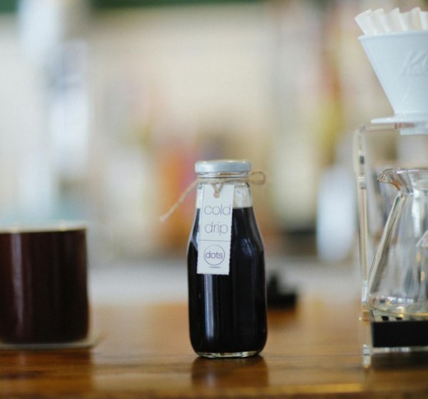 Coffee on a table three ways: in a cup, in a bottle, being made from a percolator.