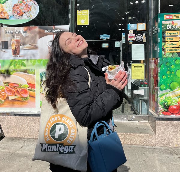 Woman holding vegan sandwich in front of a bodega.